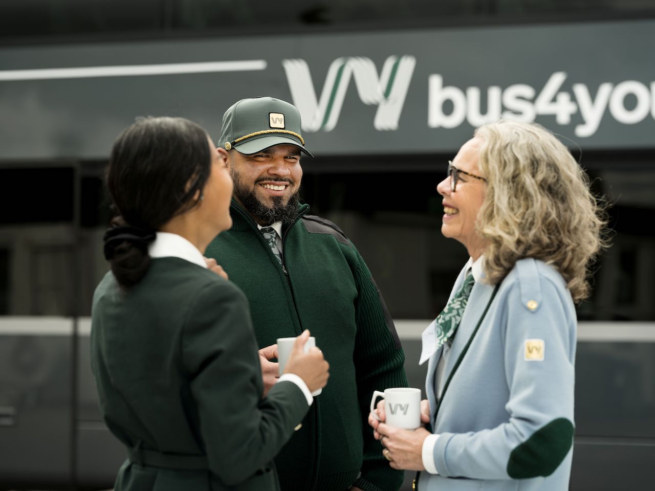 Medarbetare på Vy som skrattar och dricker kaffe framför en buss